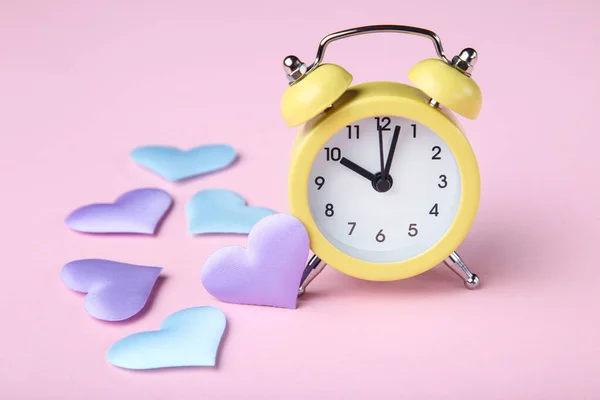 Yellow alarm clock with colorful hearts on pink background