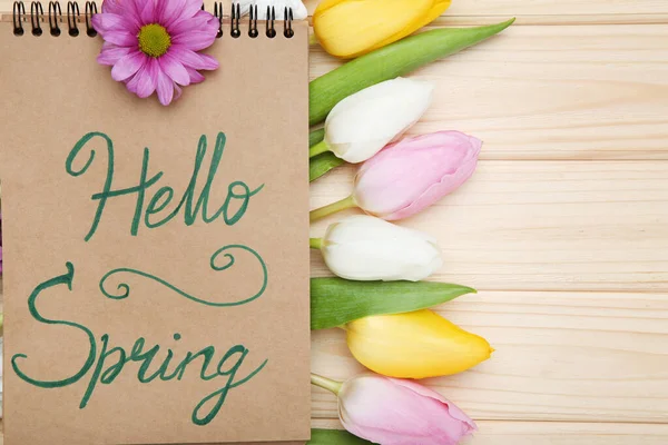 Tulip, chrysanthemum flowers and notepad with text Hello Spring on wooden table
