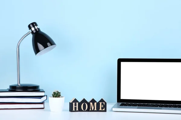 Laptop computer with books, cactus and electrical lamp on blue background