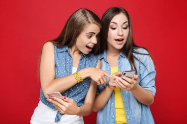 Kırmızı arka planda cep telefonu olan genç kız arkadaşlar