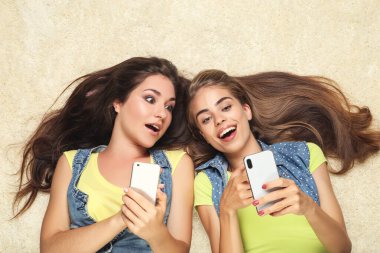 Cep telefonları halının üzerinde duran mutlu genç kız arkadaşlar.