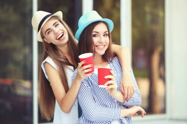 Sokakta kağıt bardakları olan iki mutlu genç kız arkadaş.