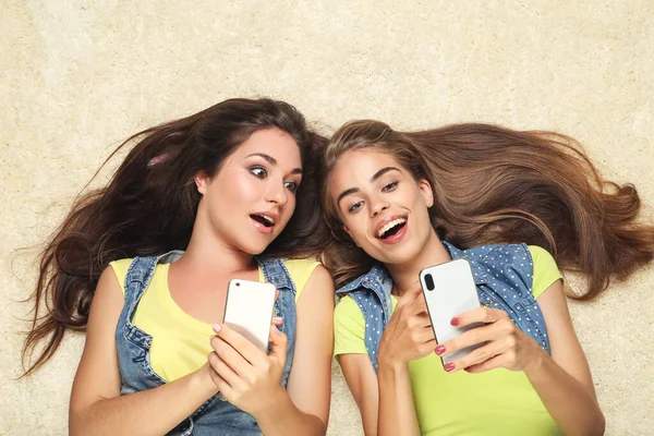 Cep telefonları halının üzerinde duran mutlu genç kız arkadaşlar.