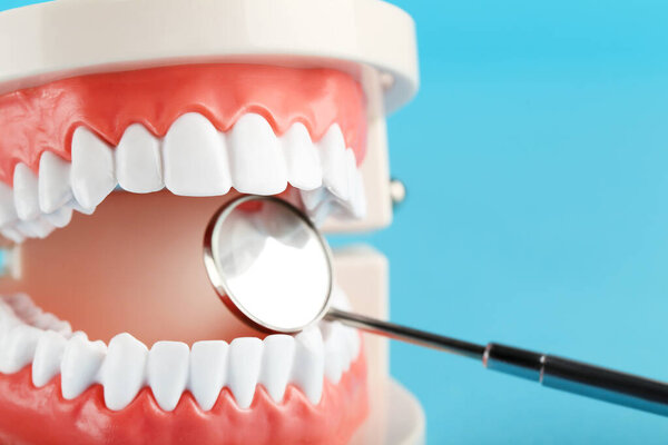 Teeth model with dental mirror on blue background