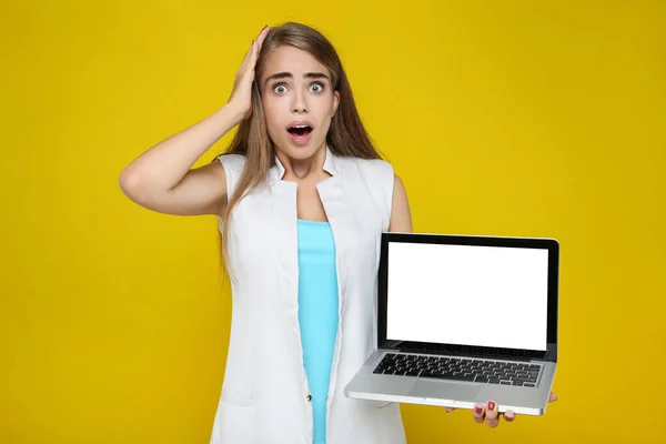 Surprised woman holding laptop computer on yellow background