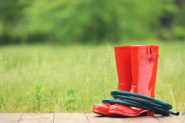 Sepatu Karet Merah Dengan Selang Hijau Papan Kayu — Stok Foto