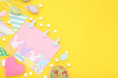 Paskalya konsepti. Sarı arka planda şekerleme, marşmelov ve yumurtalı tebrik kartı.