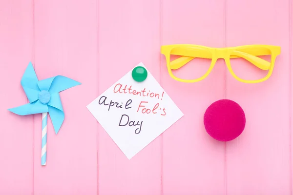 テキスト注意4月の愚か者の日ピンクの木製の背景に紙の風車と眼鏡 — ストック写真