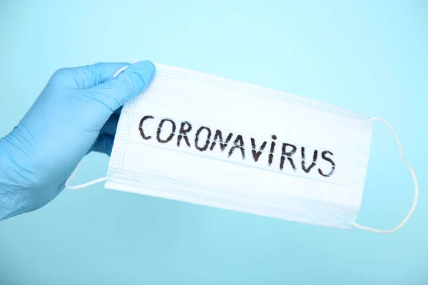 Female hand holding mask with text Coronavirus on blue background