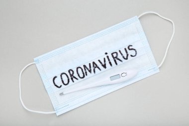Metin Coronavirus ve gri arkaplan üzerindeki temometreye sahip maske