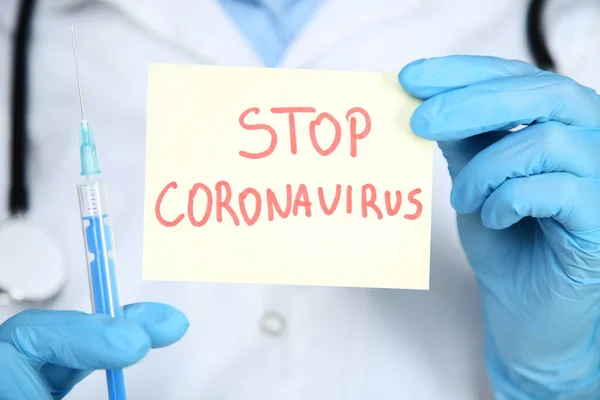 Doctor holding paper with text Stop Coronavirus and syringe