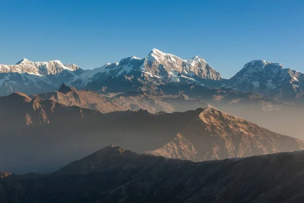 Amanecer brumoso paisaje de montañas nevadas con impresionantes colinas iluminada por el sol primero luz en los picos nevados y el primer plano en el fondo, Himalaya, Nepal. — Foto de Stock