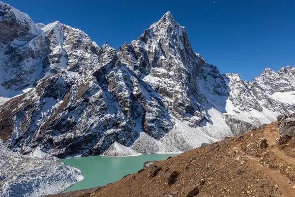 Sendero de montaña en el primer plano de un hermoso paisaje del Himalaya con pico nevado y brillante lago morrena azul y cielos azules claros . — Foto de Stock