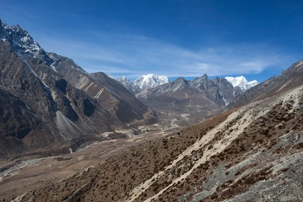 Ön plan üzerinde kahverengi rocky mountains ve ufukta beyaz karlı dağ silsilesi ile inanılmaz dağ manzarası.