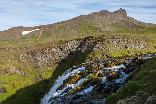 Islandia paisaje con cascada pequeña que corre entre colinas verdes y rocas cubiertas de verde brillante — Foto de Stock