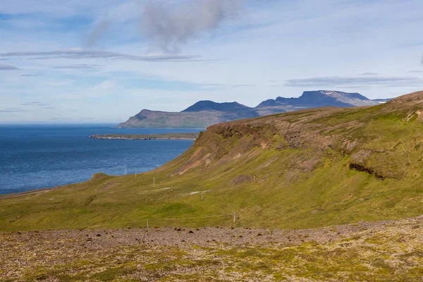 Исландский пейзаж с зелеными холмами на переднем плане и высокими скалами и Атлантическим океаном на — стоковое фото