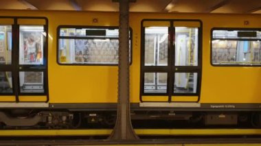 Berlin metrosundaki sarı tren kapıları kapatıp platformu terk ediyor.