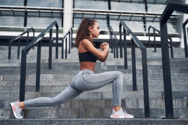 Şehir stadyumunda esneyen genç atletik kadın, şehir merkezinde antrenman yapıyor.