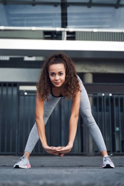 Şehir stadyumunda esneyen genç atletik kadın, şehir merkezinde antrenman yapıyor.