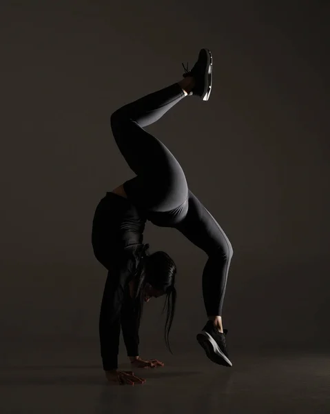 Young athletic woman making yoga and gymnastics stretching exercises on dark dramatic background with one light — 스톡 사진