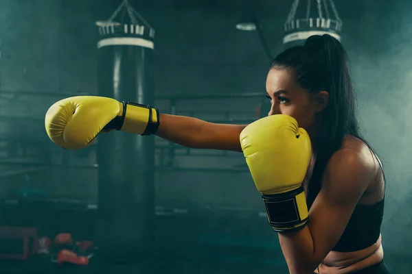 Action shot of young athletic woman training with punching bag wearing yellow boxing gloves