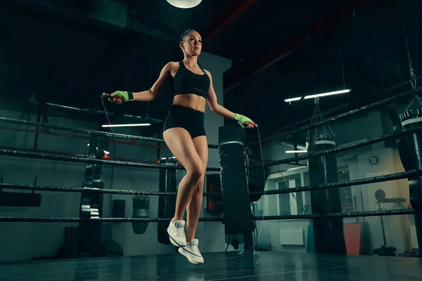 Entrenamiento de mujer atlética joven con cuerda de salto en el anillo de boxeo con vendajes de lucha —  Fotos de Stock
