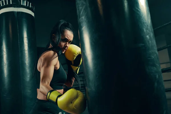 Acción de entrenamiento de mujer atlética joven con saco de boxeo usando guantes de boxeo amarillos —  Fotos de Stock