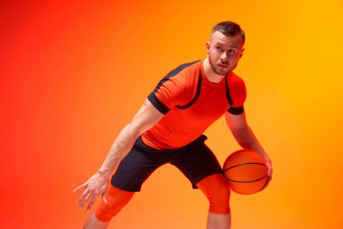 Genç atletik adam, basketbol oyuncusu turuncu ve kırmızı arka planda savunma pozisyonunda duruyor.