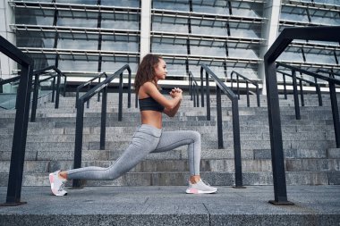 Şehir stadyumunda esneyen genç atletik kadın, şehir merkezinde antrenman yapıyor.