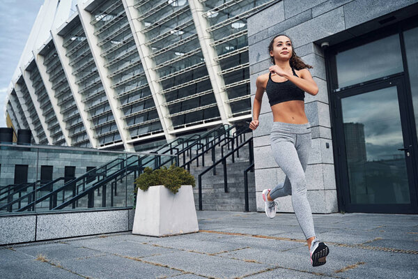 Young athletic woman running at the city stadium with urban stairs background