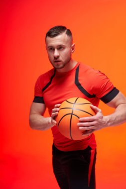 Genç atletik basketbolcu saldırı pozisyonunda iki eli turuncu ve kırmızı arka planı dumanlı topu tutuyor.