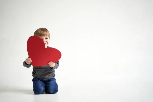 Dulce niño sosteniendo el corazón de papel rojo sobre fondo blanco. San Valentín o cuidado de niños, concepto médico —  Fotos de Stock