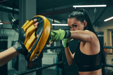 Athletic woman during fight training on boxing ring wearing green bandages on hands, punching exercises with coach