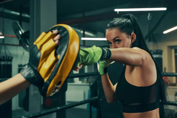 Mujer atlética durante el entrenamiento de lucha en el ring de boxeo con vendajes verdes en las manos, ejercicios de puñetazos con el entrenador —  Fotos de Stock