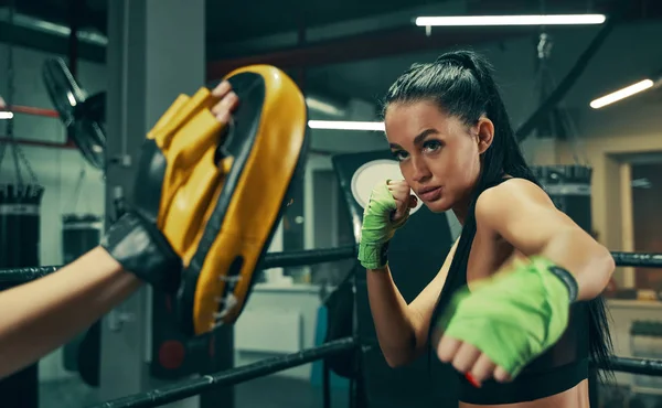Mujer atlética durante el entrenamiento de lucha en el ring de boxeo con vendajes verdes en las manos, ejercicios de puñetazos con el entrenador —  Fotos de Stock