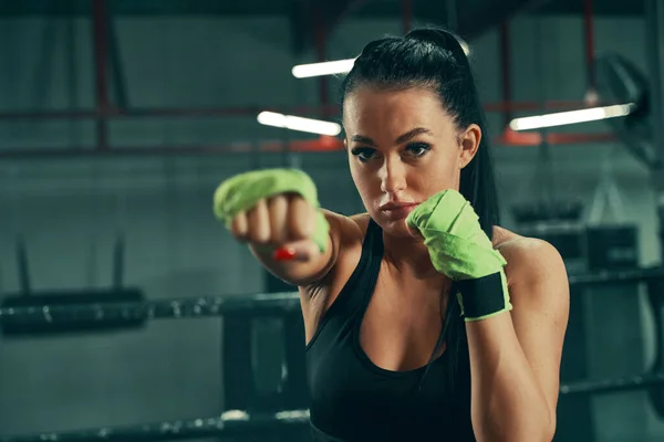 Mujer atlética durante el entrenamiento de lucha en el ring de boxeo con vendajes verdes en las manos —  Fotos de Stock