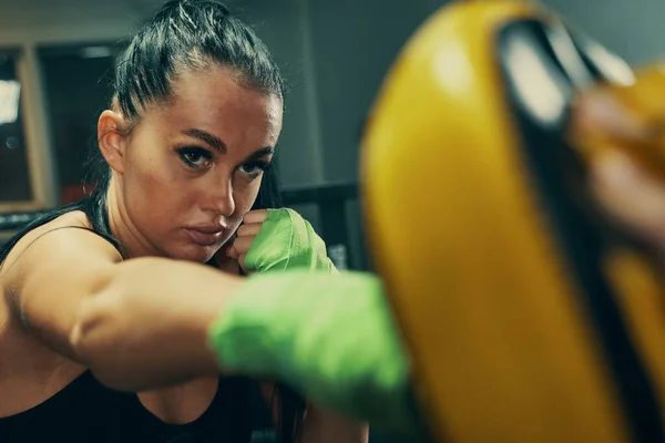 Mujer atlética durante el entrenamiento de lucha en el ring de boxeo con vendajes verdes en las manos, ejercicios de puñetazos con el entrenador —  Fotos de Stock