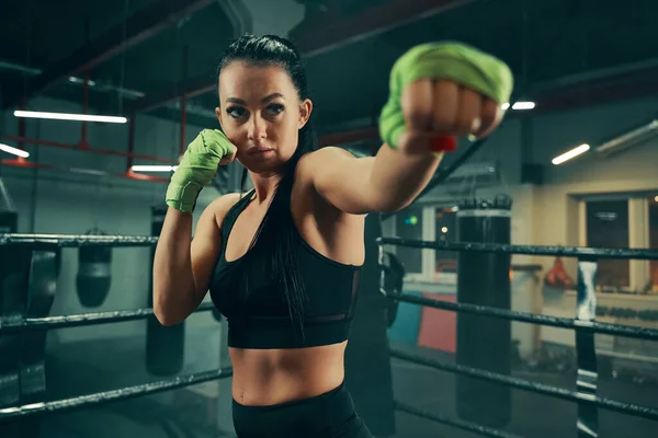 Mujer atlética durante el entrenamiento de lucha en el ring de boxeo con vendajes verdes en las manos —  Fotos de Stock