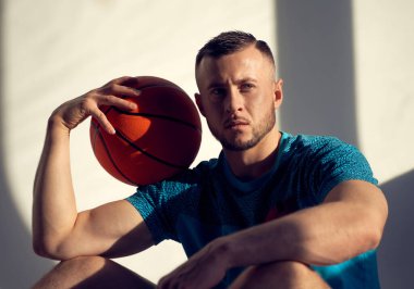 Basketbolcunun portresi omuzunda top tutuyordu ve duvarın yanında oturuyordu.