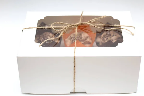 Box tied with a rope with a transparent lid with chocolate cupcakes with cream top and crispy topping in paper on a white background — 스톡 사진