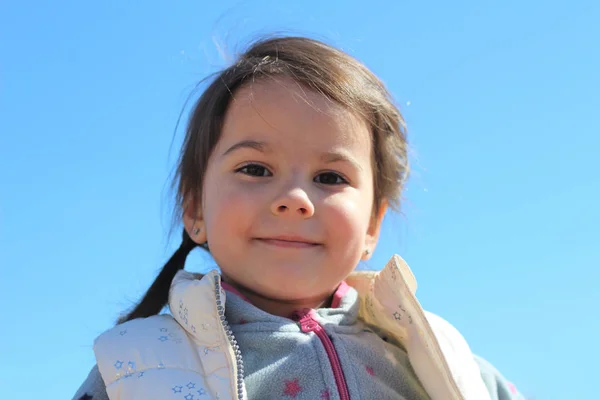 Menina sorridente bonita em um fundo de céu azul — Fotografia de Stock