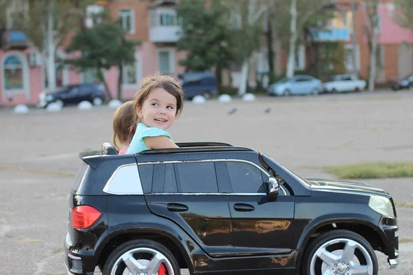 两个惊人的女孩乘坐一辆大型玩具车在城市街道上的沥青 在一个对孩子们有吸引力的夏天 在户外开车 — 图库照片