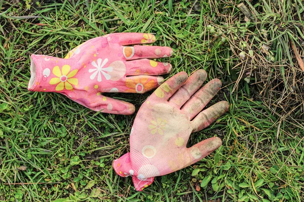 Dirty colored pink female garden gloves lie on the green grass.