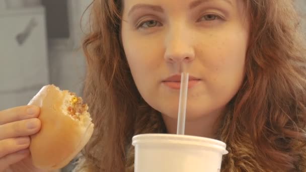 Menina bonita tentadoramente comer hambúrguer e beber refrigerante . — Vídeo de Stock