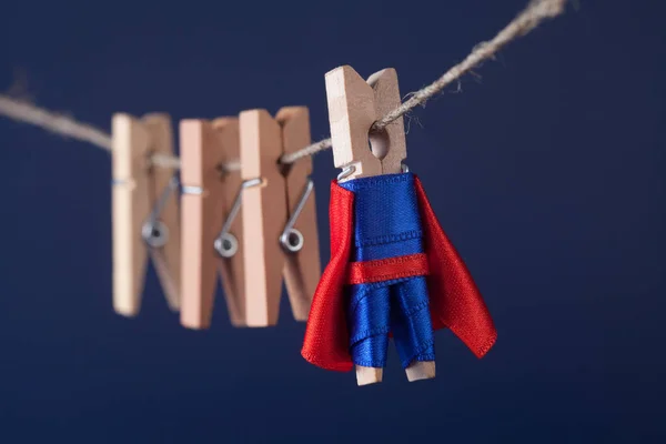 Powerful superstar peg character in blue suit red cape. leadership and wooden clothespins team at work. Dark background. soft focus. macro view