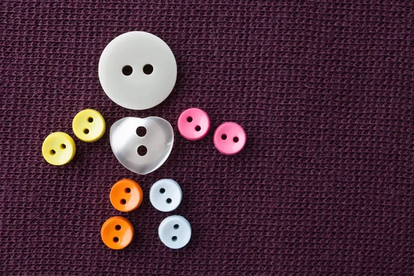 Funny character made of colorful sewing buttons with love heart shape central button. violet textured textile background. macro view, shallow depth of field