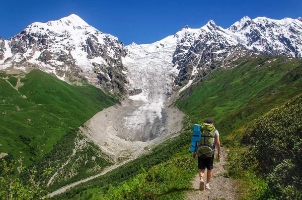 Tourist with large backpack rises on mountain trail with view of the Lardaard ice-fall in Georgia Svaneti — Stock Photo, Image