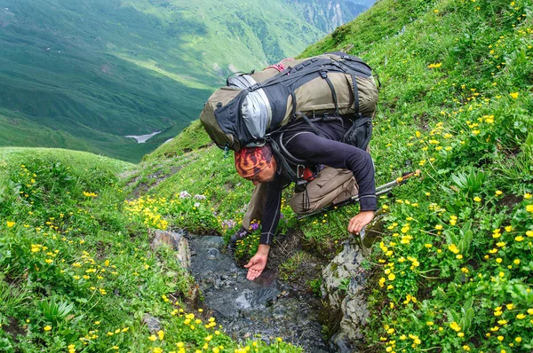 Hiker young man with backpack drinking water from stream with hands. — Stock Photo, Image