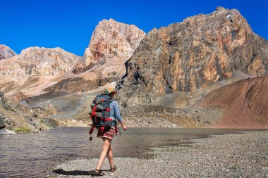 Bir sırt çantası bir kızla fan dağlarda Göl boyunca yol gösterir. Tacikistan