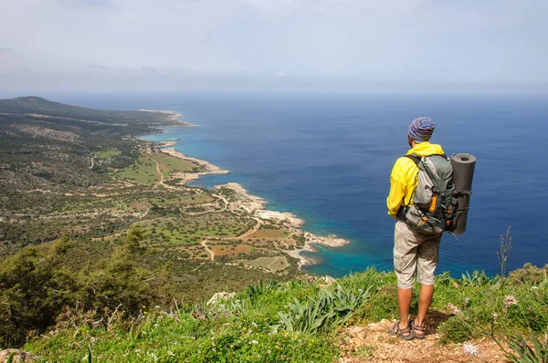 Man with a backpack stands on the shore of the Mediterranean Sea and looks into the distance Stock Image